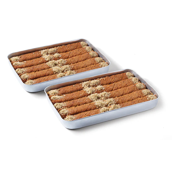 A rectangular metal baking pan filled with rolled cinnamon sticks or baklava, topped with chopped nuts, on a plain white background.