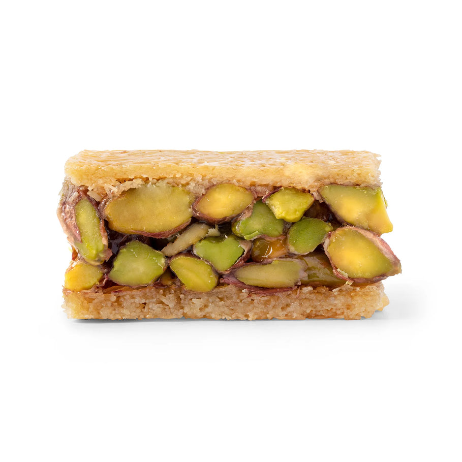 A rectangular metal tray holding several cut pieces of baklava or pastry, arranged in rows and topped with a green pistachio-like filling, photographed on a clean white background.